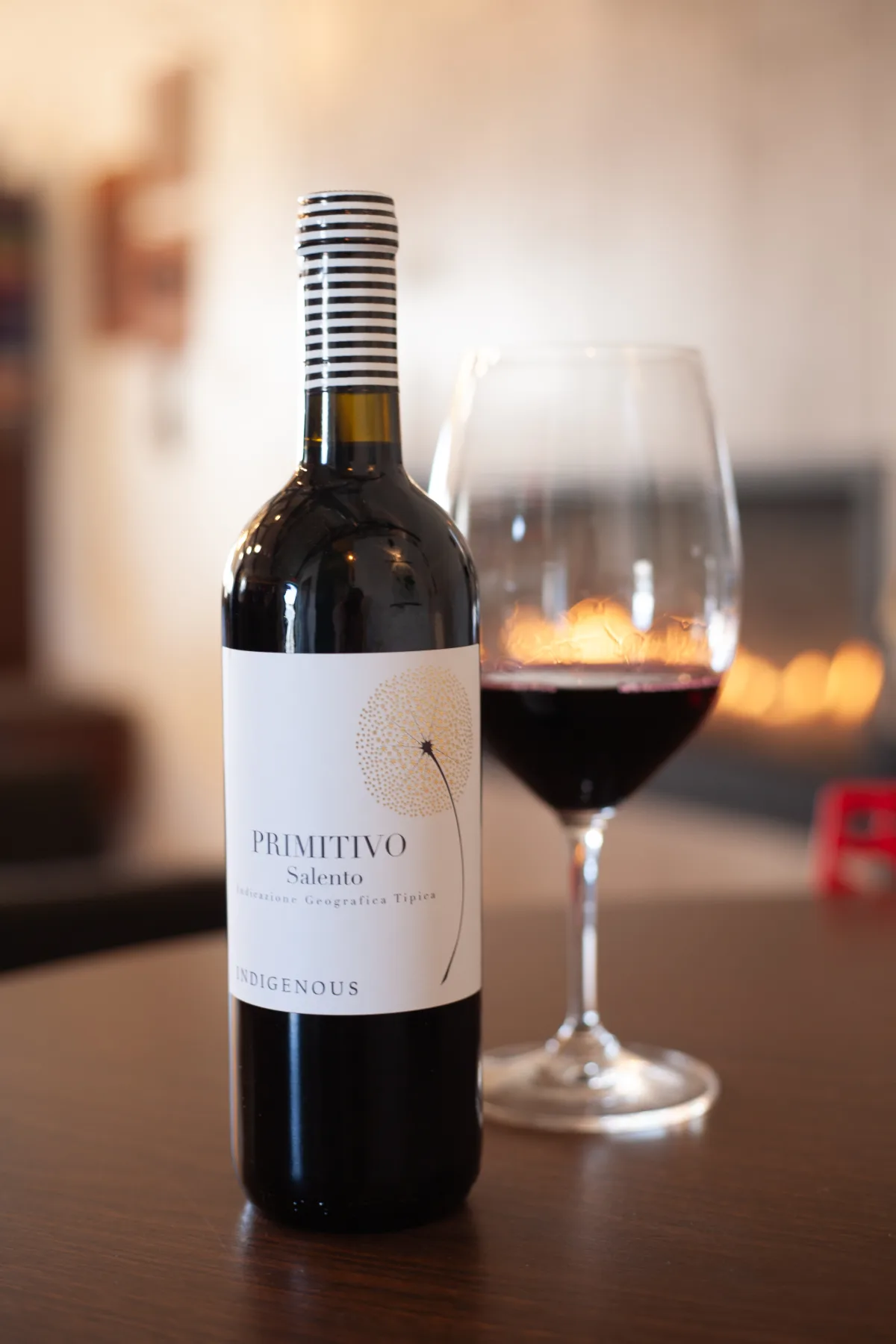 Bottle of Primitivo Salento red wine beside a poured glass by the fireplace at Adesso